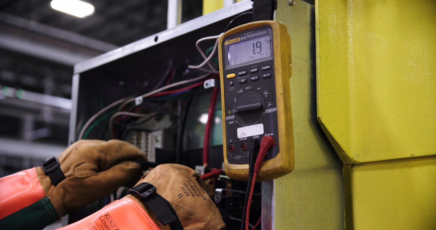 Technician in insulated gloves testing energized equipment with a multimeter